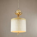 Elegant pendant light with cream drum shade, gold coral accents, and a silver orb against a neutral background.