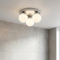Modern chrome flush ceiling light with four frosted glass globes mounted in a bathroom with grey tiled walls.