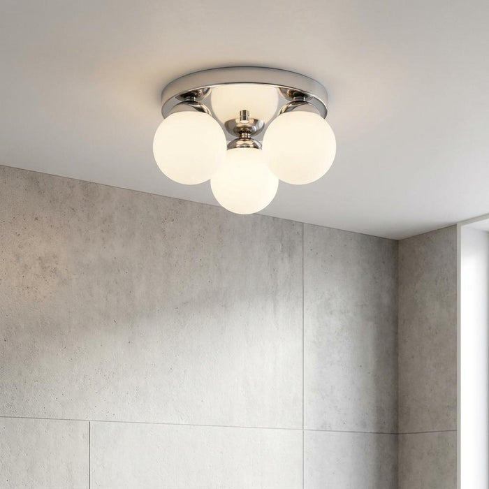 Modern chrome flush ceiling light with four frosted glass globes mounted in a bathroom with grey tiled walls.