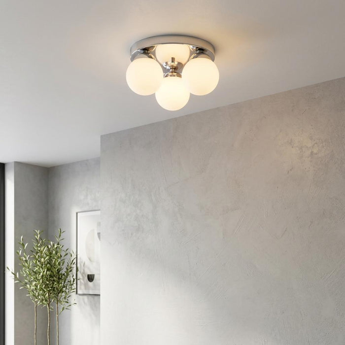 A modern chrome flush ceiling light with four white globe shades glowing on a white ceiling in a contemporary room.