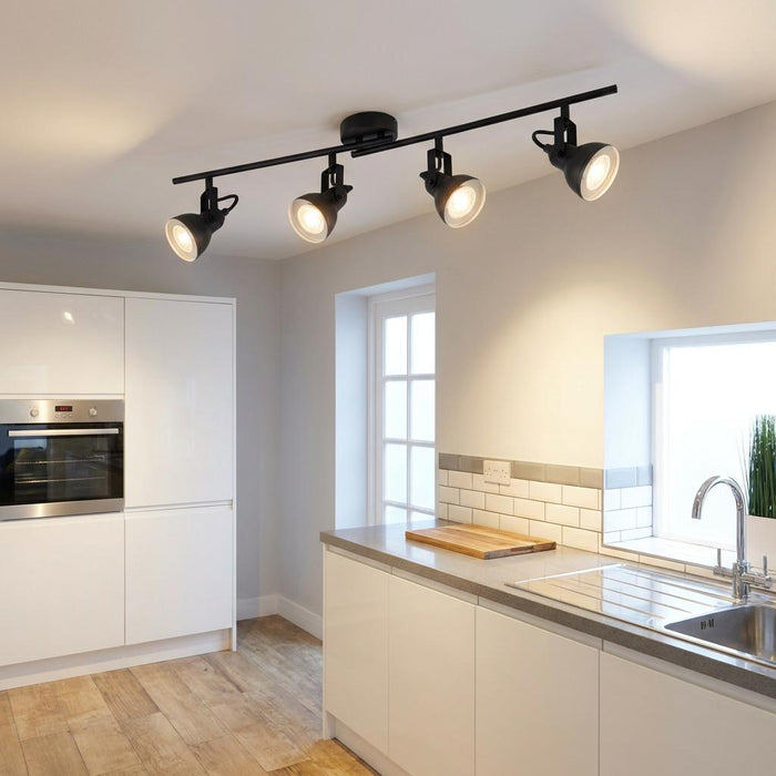 Four black adjustable spotlights on a ceiling bar illuminate a modern white kitchen.