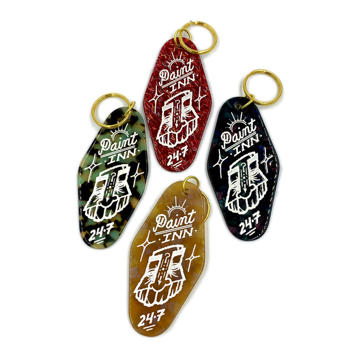 Set of five GATS "Paint INN 24.7" keychains by GATS, each in a different color (red, green, black, brown, blue) with gold key rings and a white graphic featuring the iconic hand holding a paintbrush—ideal for fans of vintage-inspired acrylic keychains with nostalgic flair.