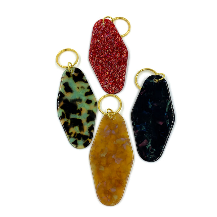 Introducing the GATS - "Paint INN 24.7" Keychains: a set of four uniquely shaped acrylic keychains by GATS, each with a gold ring and its own distinct pattern—red glitter, green and black tortoiseshell, dark multicolor, and amber marbled—that add a playful twist to the traditional vintage motel keychain style.