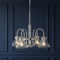Chrome chandelier with four clear glass cone shades lit against a dark navy blue paneled wall.