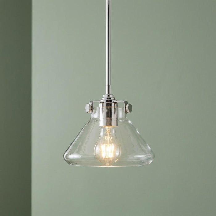 Hinkley Congress chrome pendant light featuring a clear glass tapered shade and glowing bulb against a green wall.