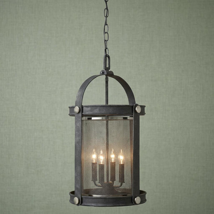 Industrial zinc hanging lantern with four lit bulbs and a mesh screen against a textured green wall.