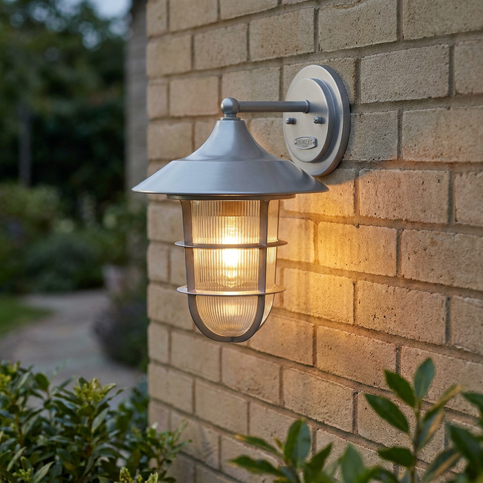 Silver Hinkley Marina outdoor wall lantern with ribbed glass glowing against a light brick wall.