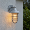 Silver nautical-style wall lantern with ribbed glass and a warm glow mounted on a textured white exterior wall.