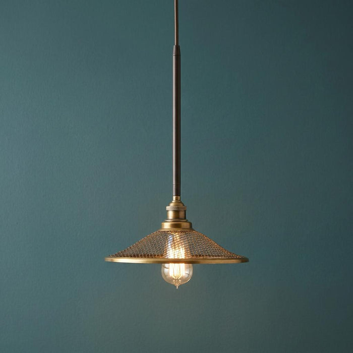 Industrial bronze pendant light with a wire mesh shade and lit Edison bulb against a dark teal wall.