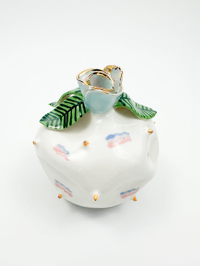 Harriet by Jen Dwyer is a round white ceramic vase with gold luster, featuring pastel pink and blue accents, gold spikes, a flower edged in gold on top, and elegant green striped leaves.