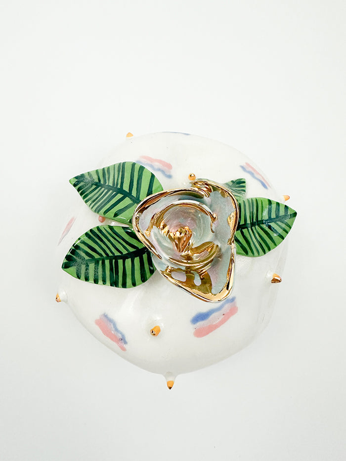 Jen Dwyers Harriet is a decorative ceramic piece featuring gold-accented flowers, green striped leaves, and pastel pink and blue abstract patterns on a white background. It is enhanced by small gold dots and reflective gold luster across its glazed surface.
