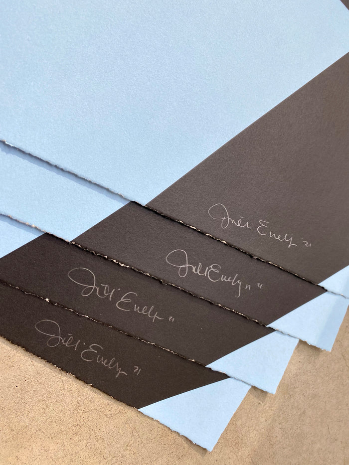 Three "Attempt" prints by Jillian Evelyn, part of a limited edition screenprint series, overlap on a surface. Each features a diagonal split design in light blue and dark gray, and is signed Jillian Evelyn in white ink. Printed on Coventry Rag, these art prints come from a signed and numbered edition.