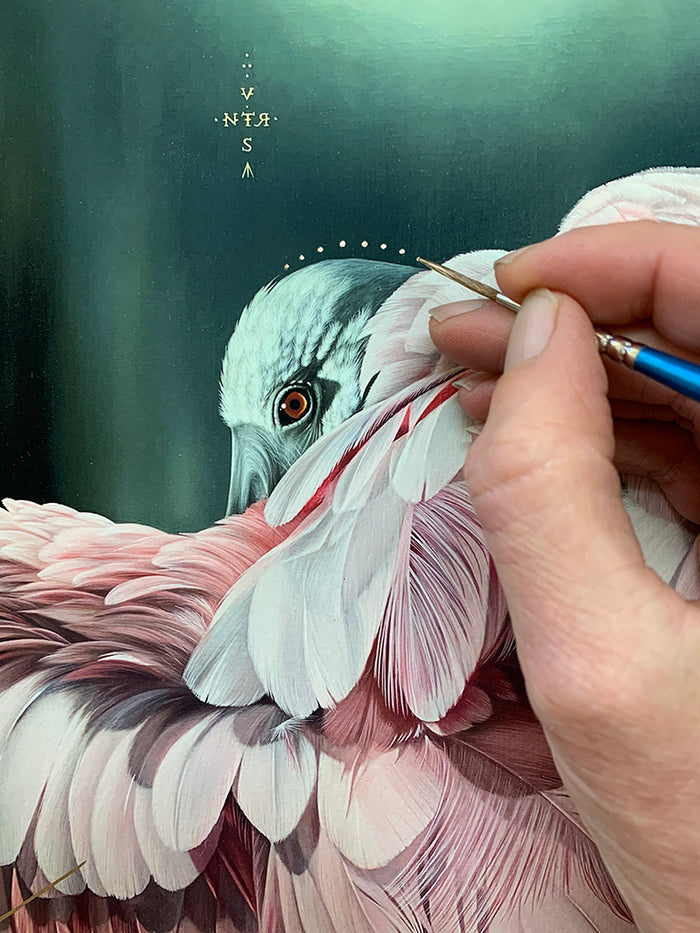 A hand holding a thin paintbrush adds detail to a realistic painting of a pink and white bird with piercing eyes, partially hidden by its feathers. Geometric symbols float above the bird’s head in "Watershed," a limited edition archival pigment print by Josie Morway, with each piece signed and numbered by the artist.