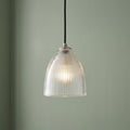Illuminated elongated prismatic glass pendant light with a ribbed texture hanging against a sage green wall.