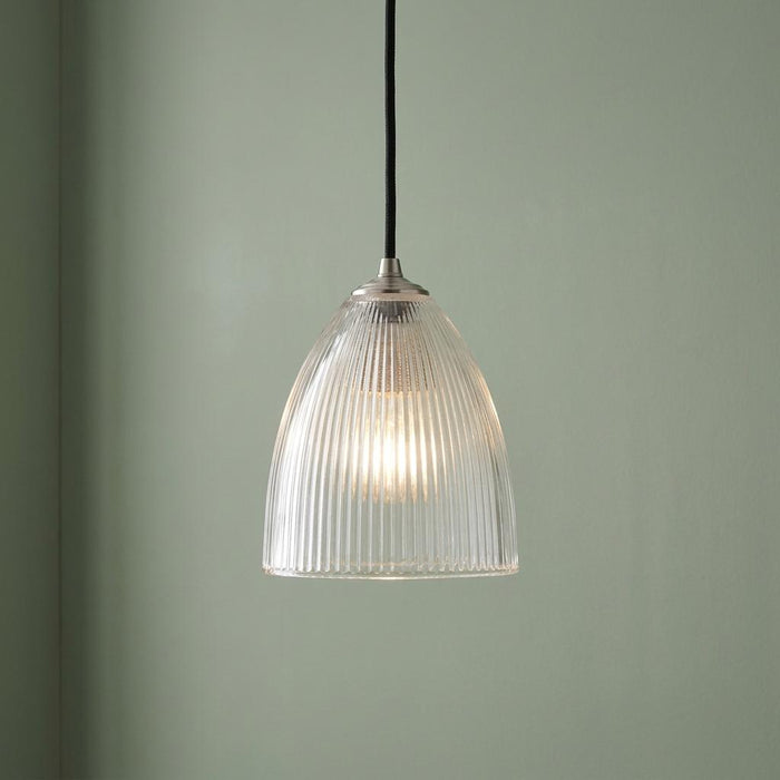 Illuminated elongated prismatic glass pendant light with a ribbed texture hanging against a sage green wall.