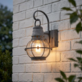 Kichler Bridge Point zinc outdoor lantern with seeded glass globe lit on a white brick wall.