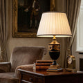 Narbonne black and gold table lamp with a pleated ivory shade on a side table in a classic living room.