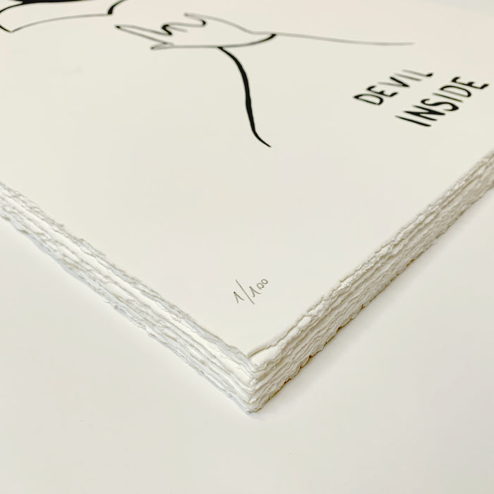 A stack of white paper with rough edges features a minimalist black line drawing of a hand on top. The screen print, titled Devil Inside by Petites Luxures, is signed and numbered 1/100 as part of this limited edition.