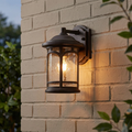 Bronze outdoor wall lantern with seeded glass and a warm glow mounted on a light-colored brick wall.