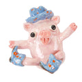 The Rootin Tootin Pig figurine by Katie Kimmel for Hashimoto Contemporary features a pink ceramic pig sitting upright with its tongue out, playfully raising its legs, and adorned with a blue hat and blue boots decorated with orange spots.