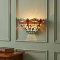 Dragonfly-patterned Tiffany wall sconce with vibrant stained glass glowing on a light green paneled wall.
