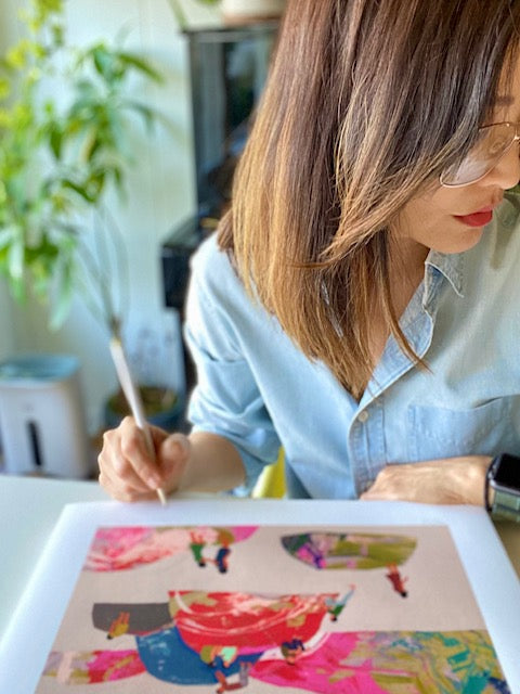 Artist Seonna Hong signing print of people standing and climbing onto rainbow colored rocks over a beige background