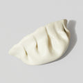 The DUMPLING by Stephanie H. Shih, features intricate folds and a glazed porcelain finish, resting on a light gray surface with a soft shadow to the right.