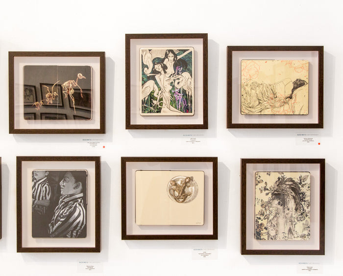 Six Sunday Morning artworks by Zachary Oldenkamp adorn a white wall in two rows, featuring botanical sketches, pen and ink abstracts, and monochrome portraits. Each piece is reminiscent of a Moleskine illustration and labeled beneath the frame.
