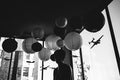 A silhouette stands by large windows amidst hanging paper lanterns and model airplanes. Buildings loom beyond in this black-and-white scene, captured in a signed and numbered archival pigment print titled “Untitled” (with Jessica Hess, San Francisco, CA), by Shaun Roberts.