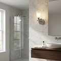 Zahira chrome bathroom wall light with a frosted glass shade on a marble wall beside a mirror.